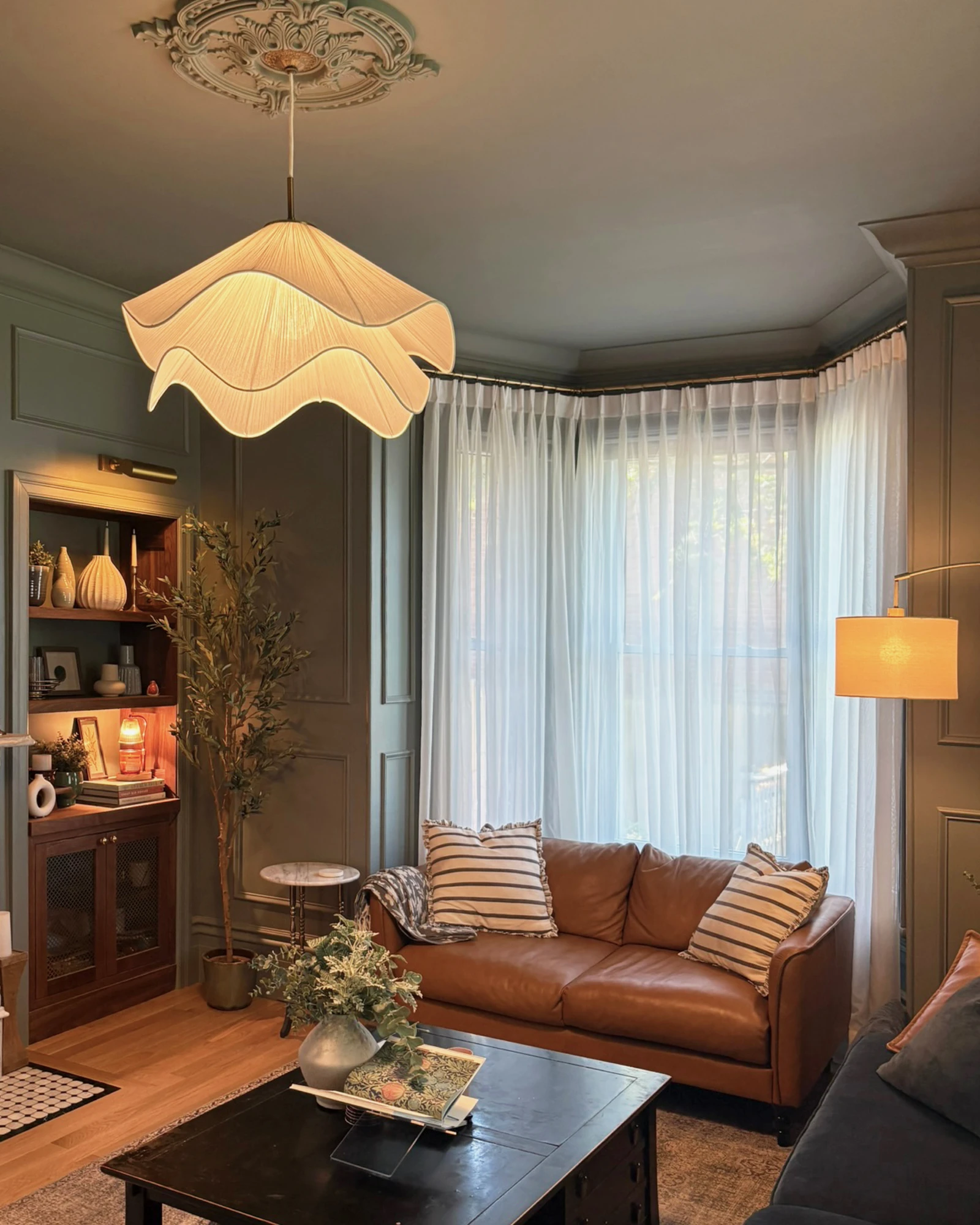 Living room seating area with a leather sofa, sheer curtains, and pendant shade