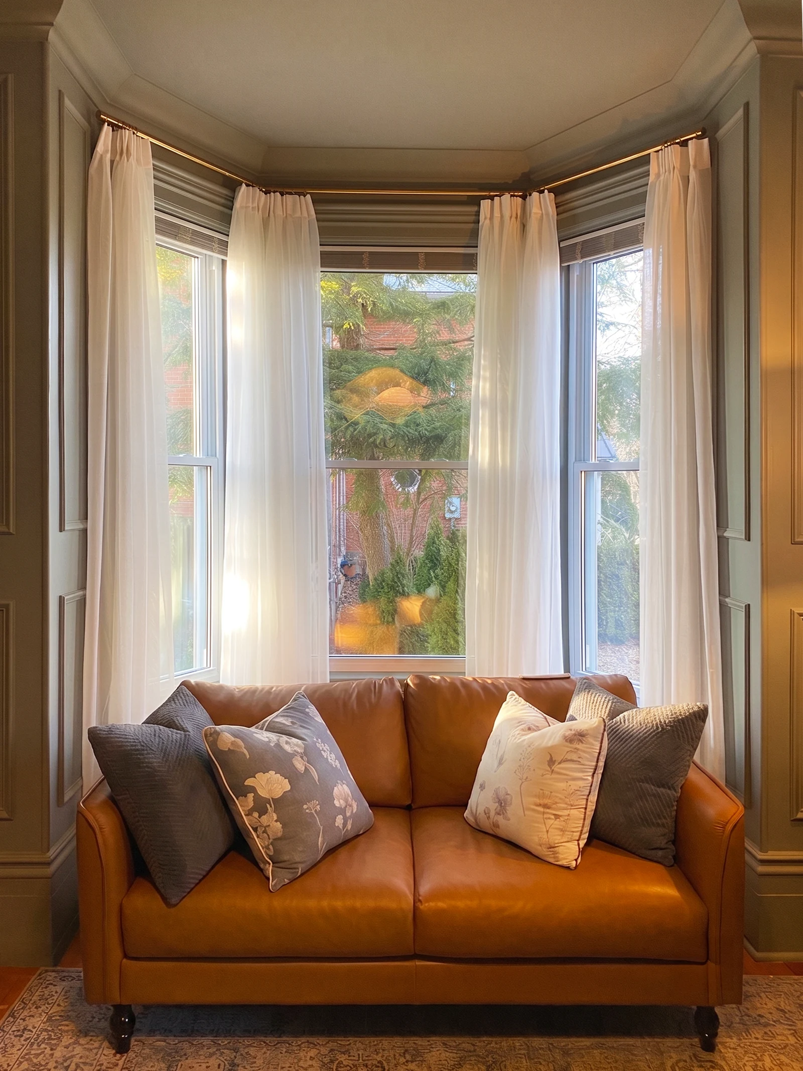 Living room sofa in a bay window with sheer drapery and warm light