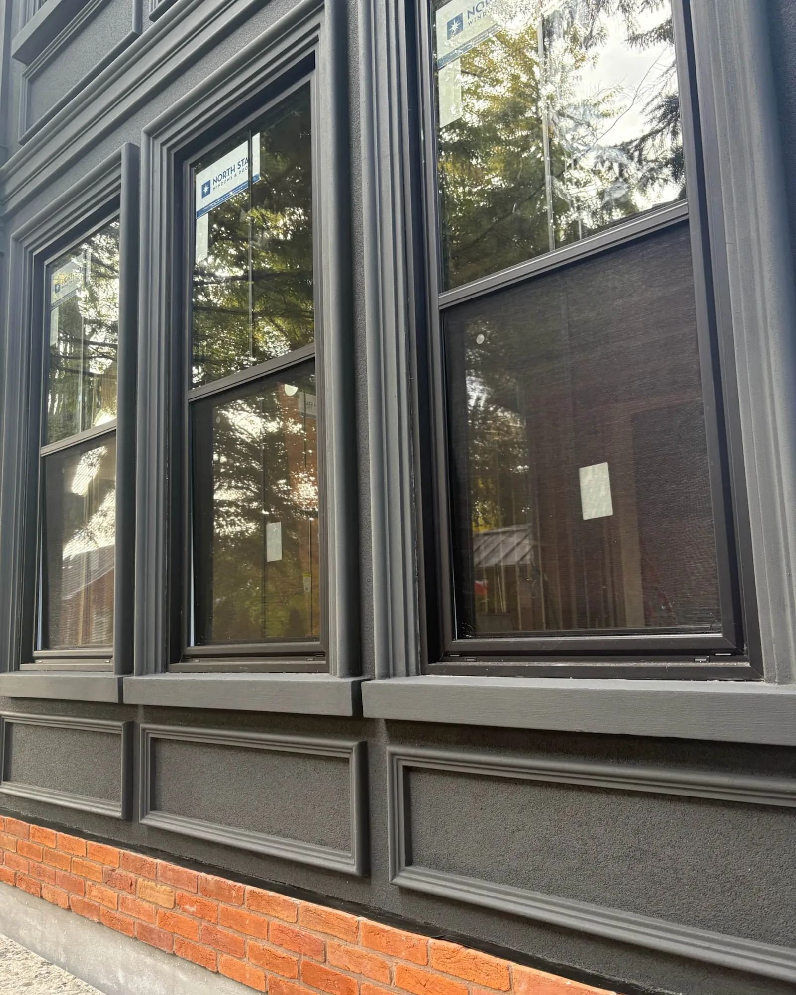 Detailed dark-painted exterior windows with historic trim above a brick foundation