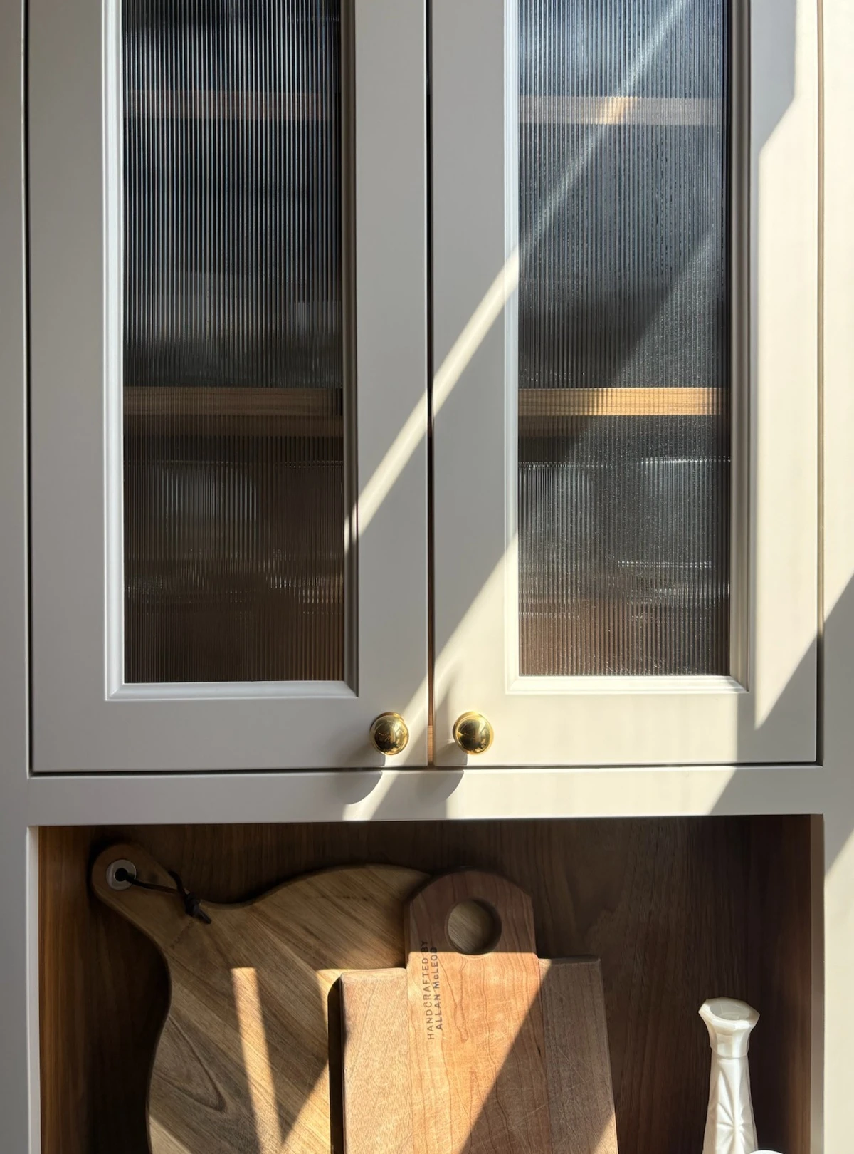 Fluted glass cabinet doors with brass knobs above an open wood shelf
