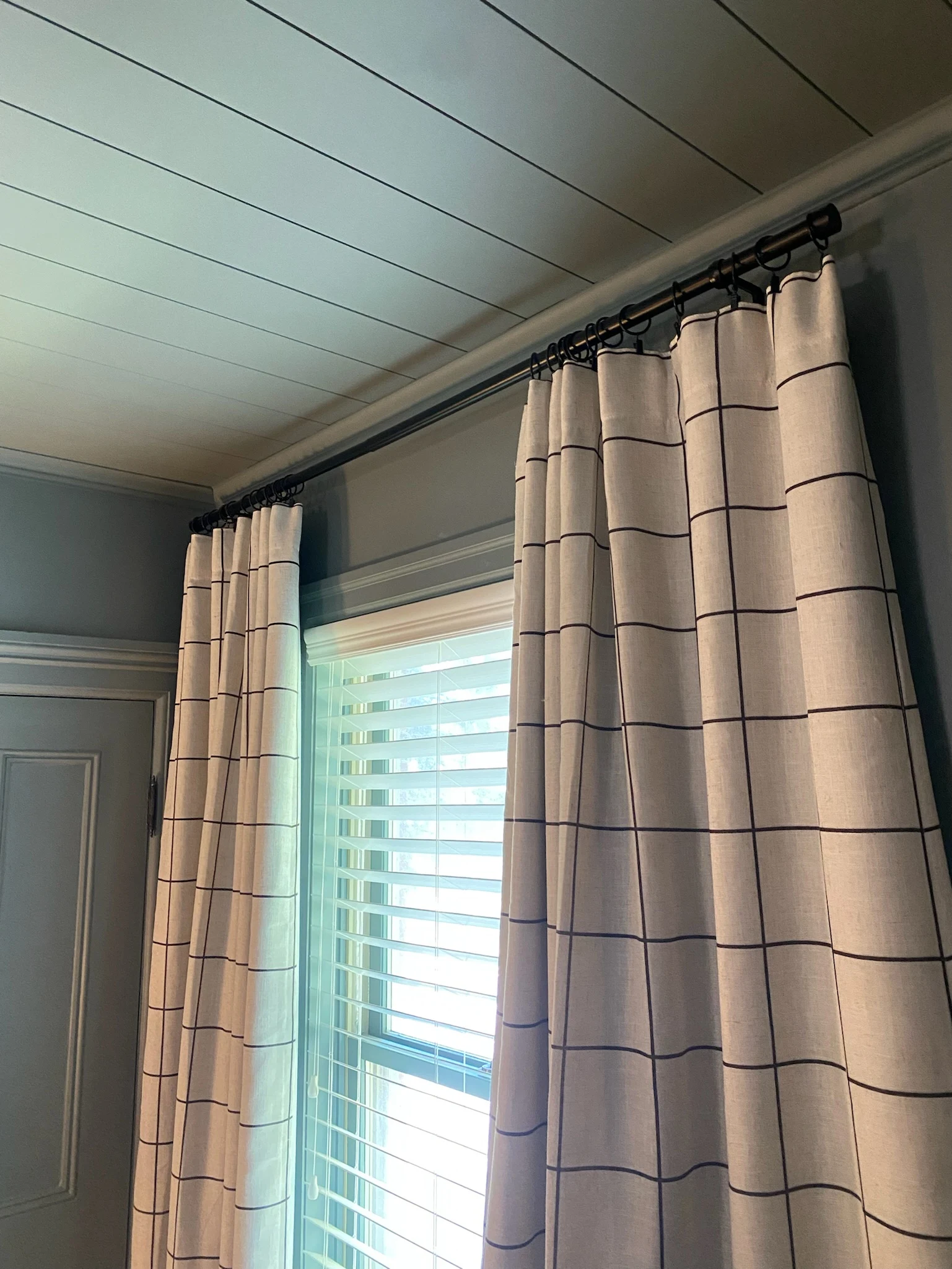 Bedroom curtain and rod detail against painted trim and paneled ceiling