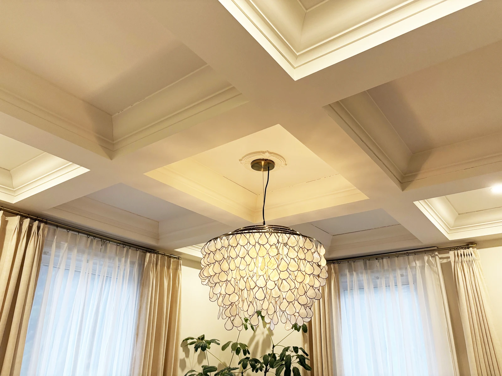 Dining room coffered ceiling, lit chandelier, and layered drapery