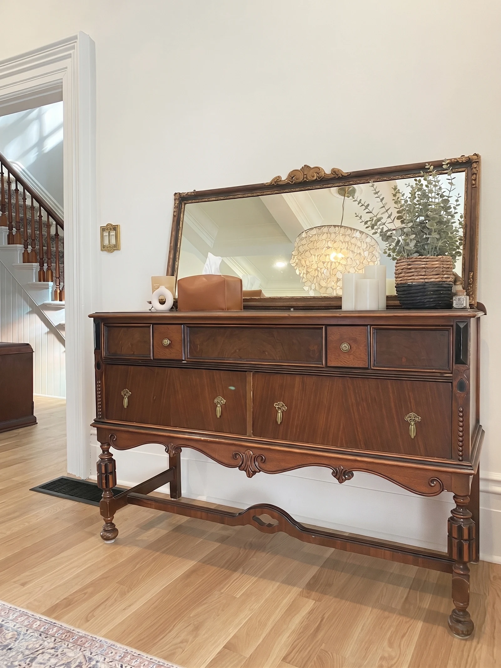 Wood sideboard with antique mirror, greenery, and dining room chandelier reflected