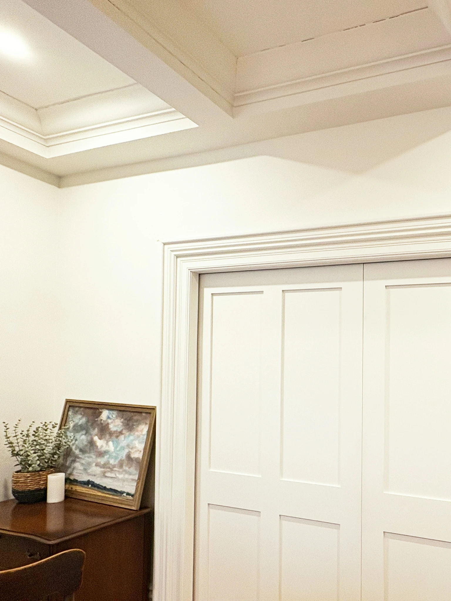 Dining room corner with coffered ceiling, paneled closet doors, sideboard, artwork, and greenery