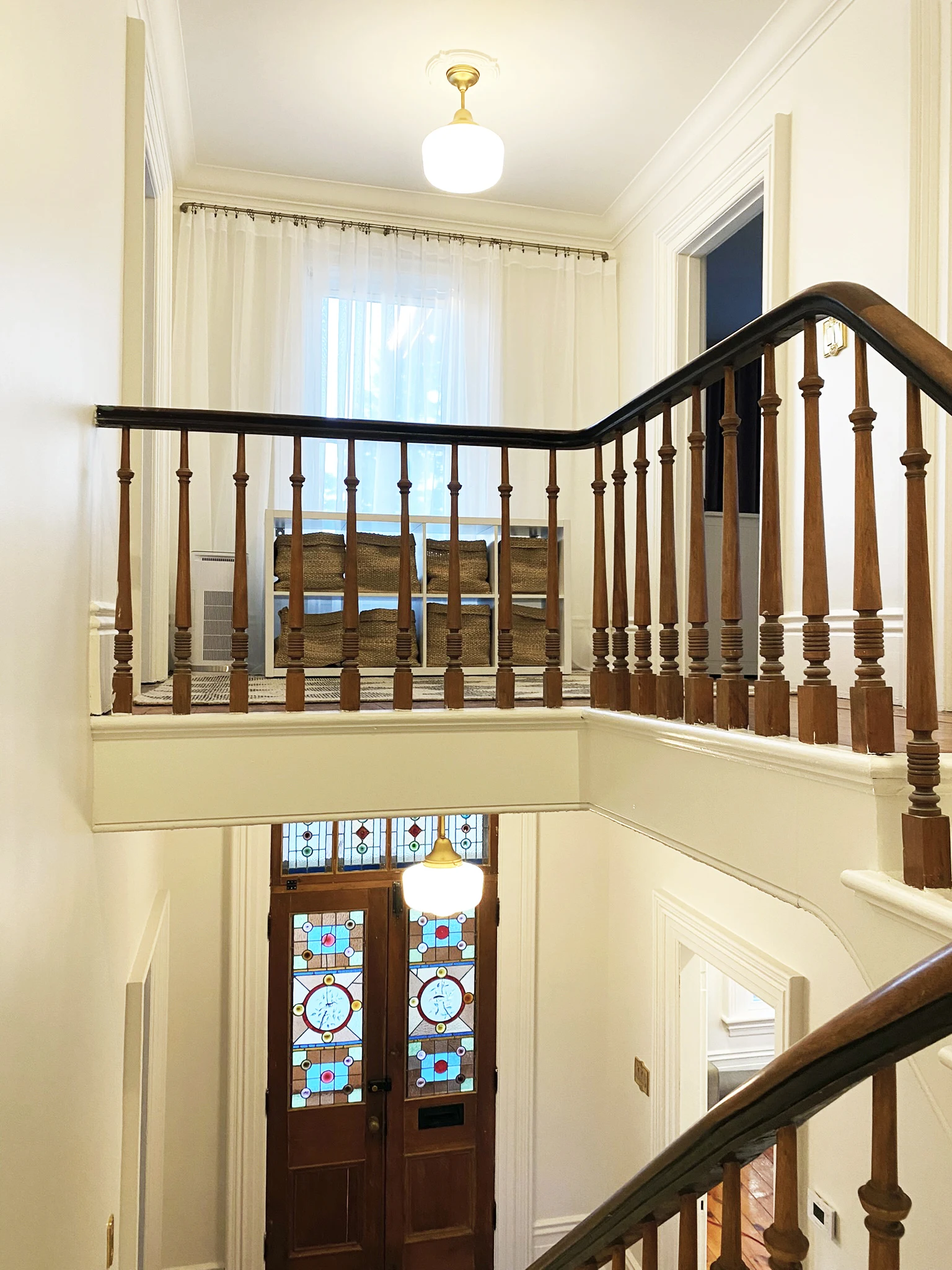Upper hallway landing with wood railing, sheer drapery, pendant lights, and stained glass entry doors