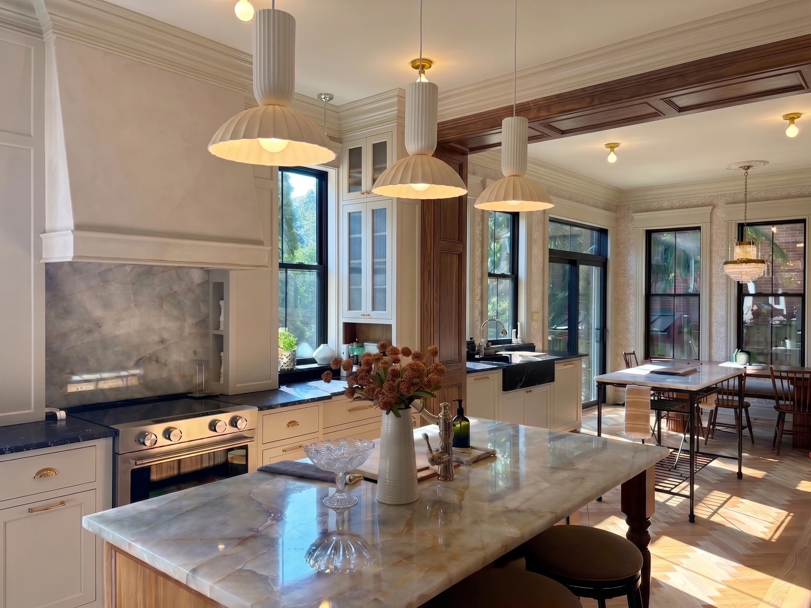 Layered kitchen with custom range hood, pendant lighting, stone island, and dining area beyond
