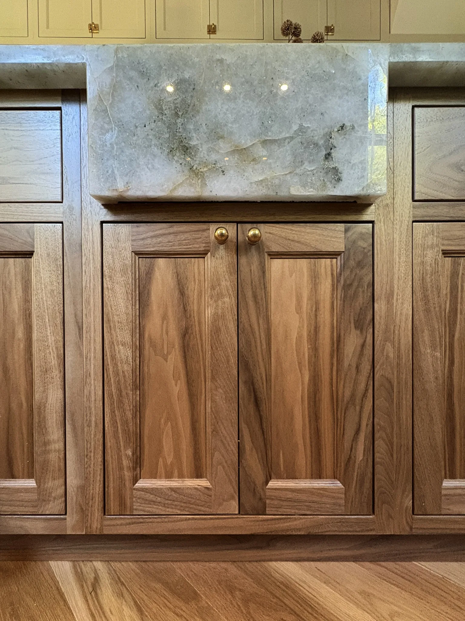 Wood kitchen cabinet detail with stone sink and brass hardware