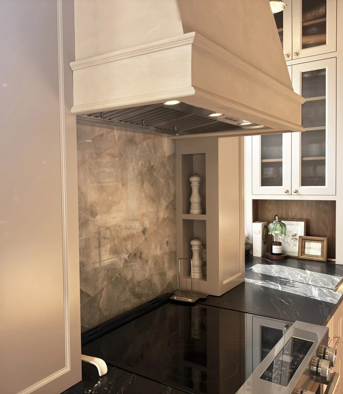 Range hood, stone backsplash, black counter, and nearby glass-front cabinetry