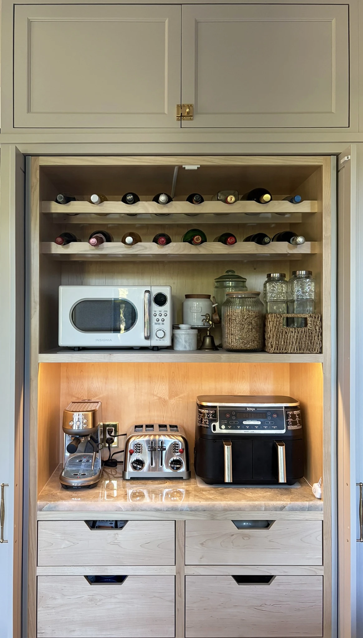 Open hidden appliance cabinet with wine storage, small appliances, drawers, and warm lighting