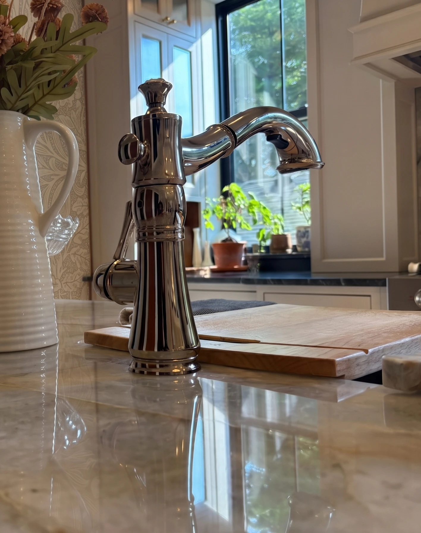 Polished kitchen faucet and marble counter detail with window garden beyond